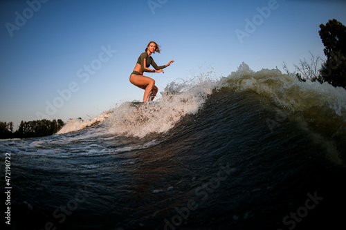 young female wakesurfer ride down the river wave against blue sky.