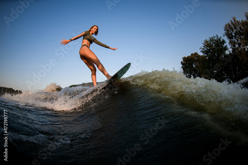 young sexy female wakesurfer ride down the river wave against blue sky.
