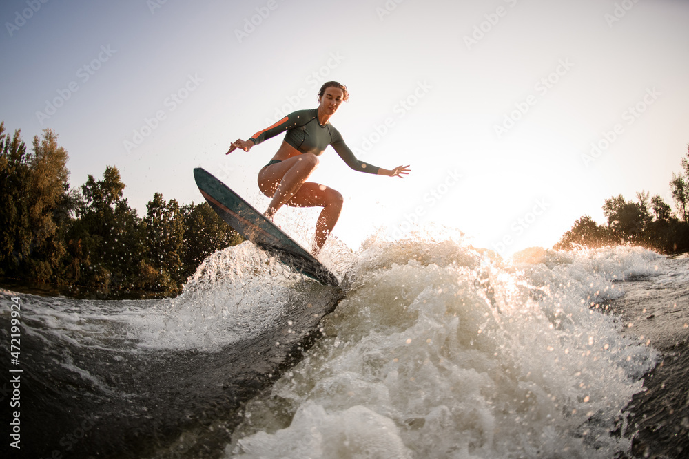 active fit woman making trick and jump with wakesurf over splashing wave.