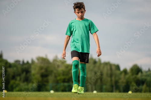 Junge mit Blick am Fußballrasen geht alleine am Fußballplatz mit Wald im Hintergrund