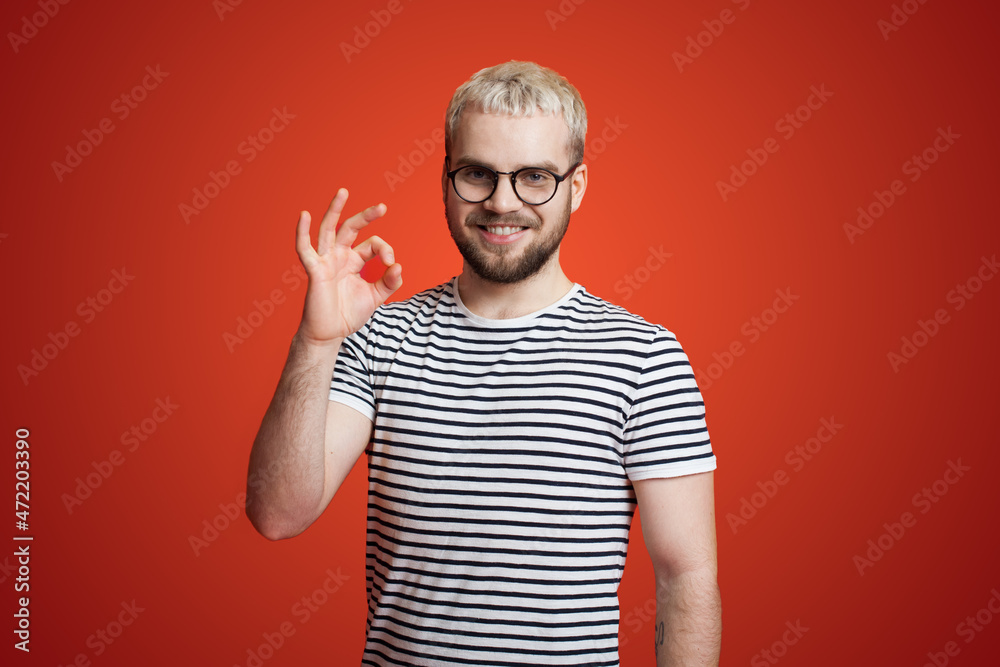 Caucasian bearded man wearing eyeglasses showing ok sign with hand and fingers isolated over red background smiling positive Caucasian bearded man wearing eyeglasses showing ok sign with hand and fingers isolated over red background smiling positive
