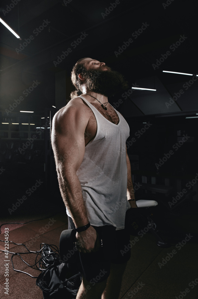 Muscular bearded man bodybuilder training in gym. Fit muscle guy workout with weights and dumbbell