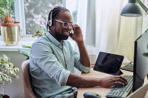 Operator of call center wearing headset sitting at his workplace and chatting with clients