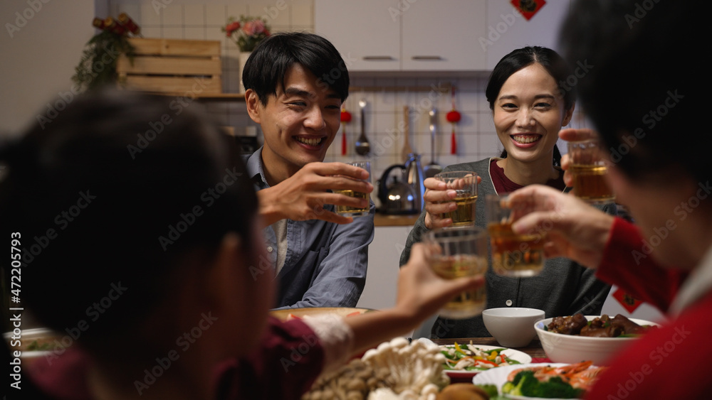 selective focus of happy young asian couple drinking toast with tea to their family at chinese lunar new year reunion dinner at home
