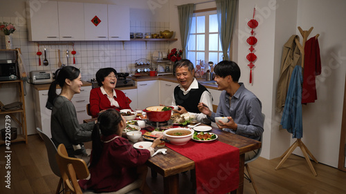 happy asian extended family laughing at the man’s joke while having reunion dinner on chinese new year’s eve in a cozy festive home interior