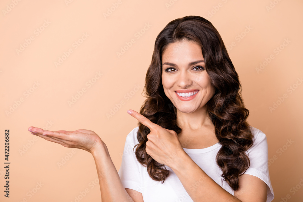 Photo of cute young curly hairdo lady hold index empty space wear white t-shirt isolated on beige color background