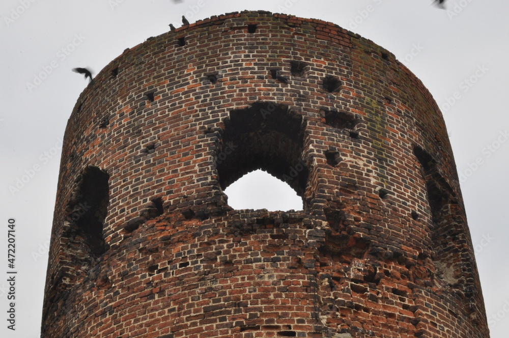 Castle ruins in Koło. Destroyed towers and defensive walls made of red brick on the bank of the Warta River. - obrazy, fototapety, plakaty 