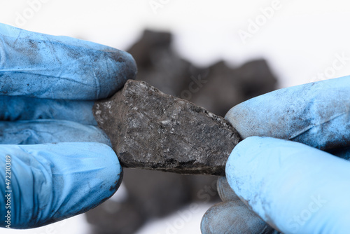 Hands in gloves hold lump of black coal in laboratory. Fossil fuel research concept.
