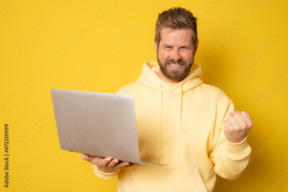 Portrait of an excited man holding laptop computer isolated on yellow background. Portrait of an excited man holding laptop computer isolated on yellow background.