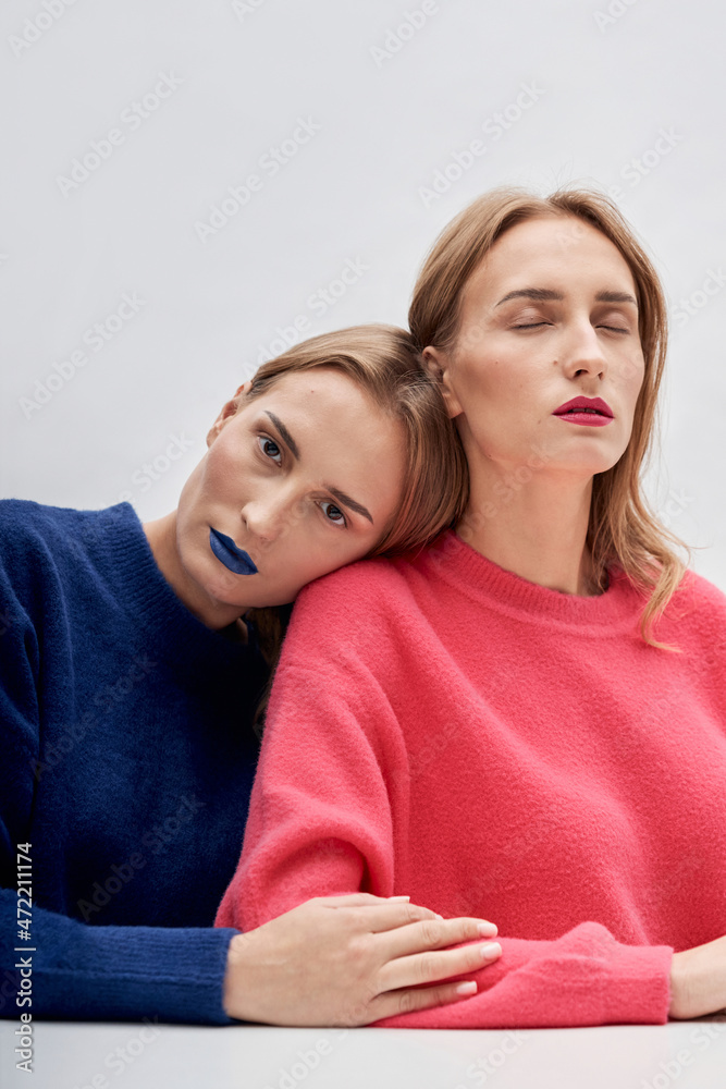 Woman with blue lipstick leaning on shoulder of twin sister against white background