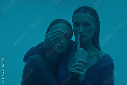 Woman covering eye of twin sister in blue fog photo