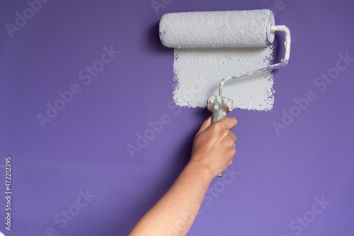 Woman hand applying light color paint to wall with roller