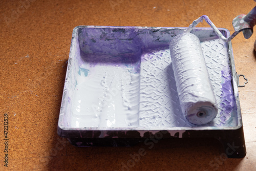 Painting roller refilling in paint tray on the floor