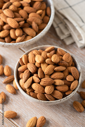 Raw almonds in bowl on wooden table background. Healthy dry nuts