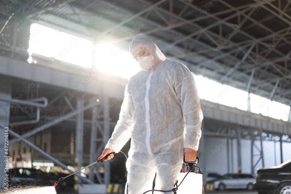 Man dressed white protective overalls spraying surface antibacterial sanitizer sprayer during quarantine Man dressed white protective overalls spraying surface antibacterial sanitizer sprayer during quarantine
