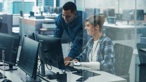 Teamwork In Diverse Inclusive Office: Project Manager Talks with Woman with Disability with Prosthetic Arm Work on Desktop Computer. Professionals Software Engineers Create e-Commerce App Solution