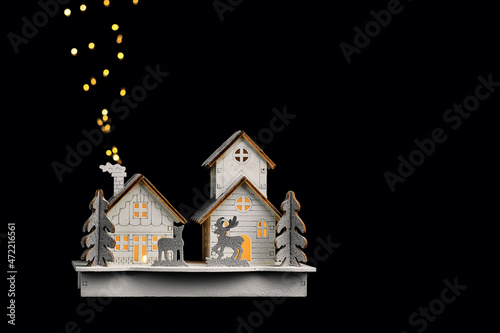 Wooden toy house with deer and fir trees on a black background