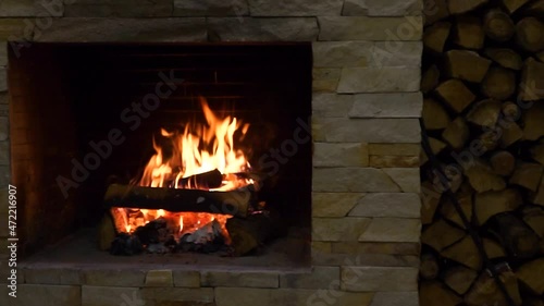 A brick fireplace in which a fire is burning. Firewood next to the fireplace 