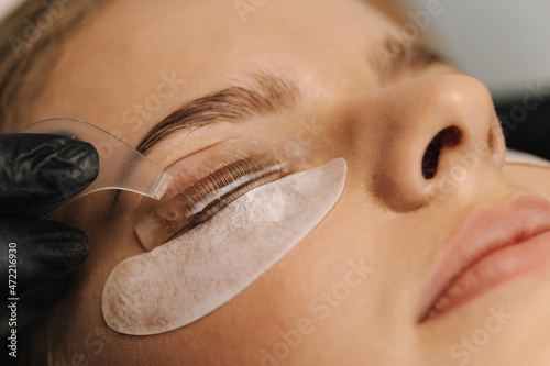 Close-up of eyelash care treatment procedures. Beautiful female, blond hair model have eyelashes lamination. Woman doing staining, curling, laminating and extension for lashes