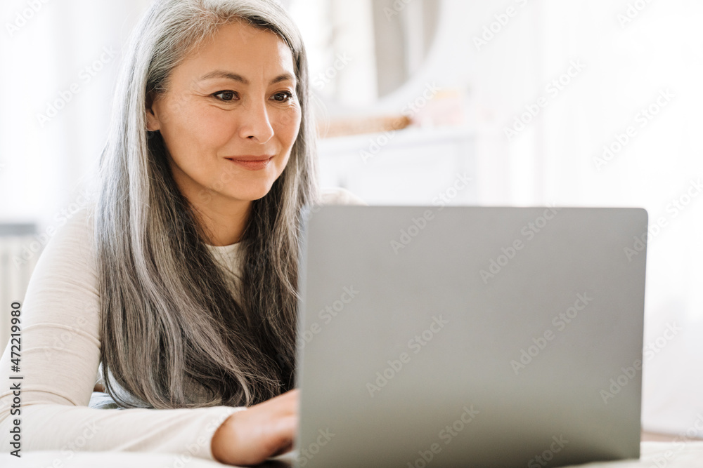 Mature asian woman with grey hair working with laptop in bedroom Mature asian woman with grey hair working with laptop in bedroom