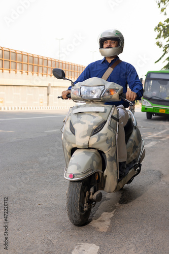 Man in helmet riding scooty on street photo