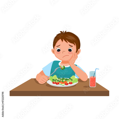 Cute little boy picky eater frustrating looking at broccoli with no appetite and refusing to eat vegetables.