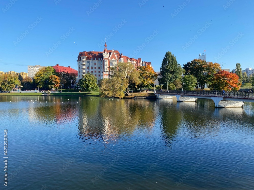Breathtaking view to The Lower Pond and a park near it in Kaliningrad city in Russia in the golden autumn season. Colorful trees and clouds reflect in the lake waters