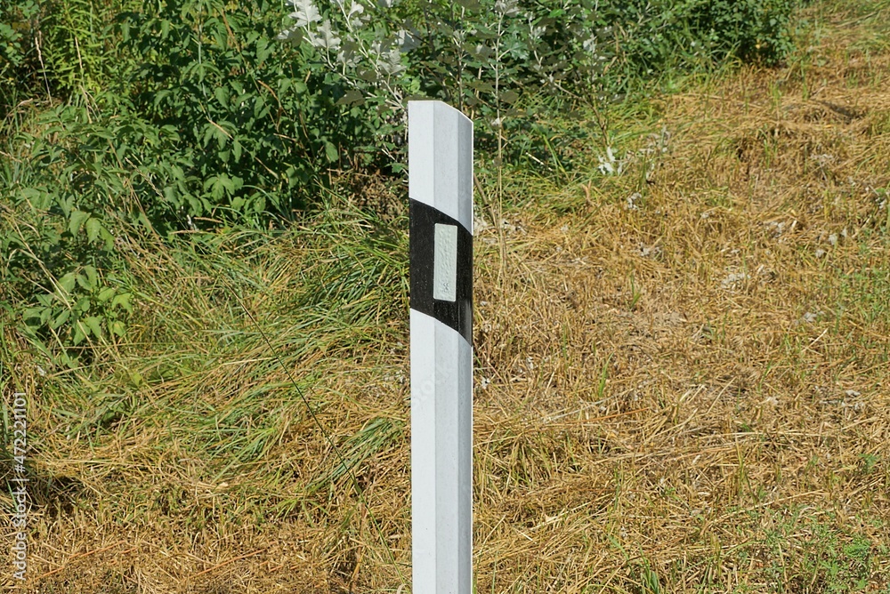 one white black metal boundary bollard with reflector stands outside in dry brown grass one white black metal boundary bollard with reflector stands outside in dry brown grass