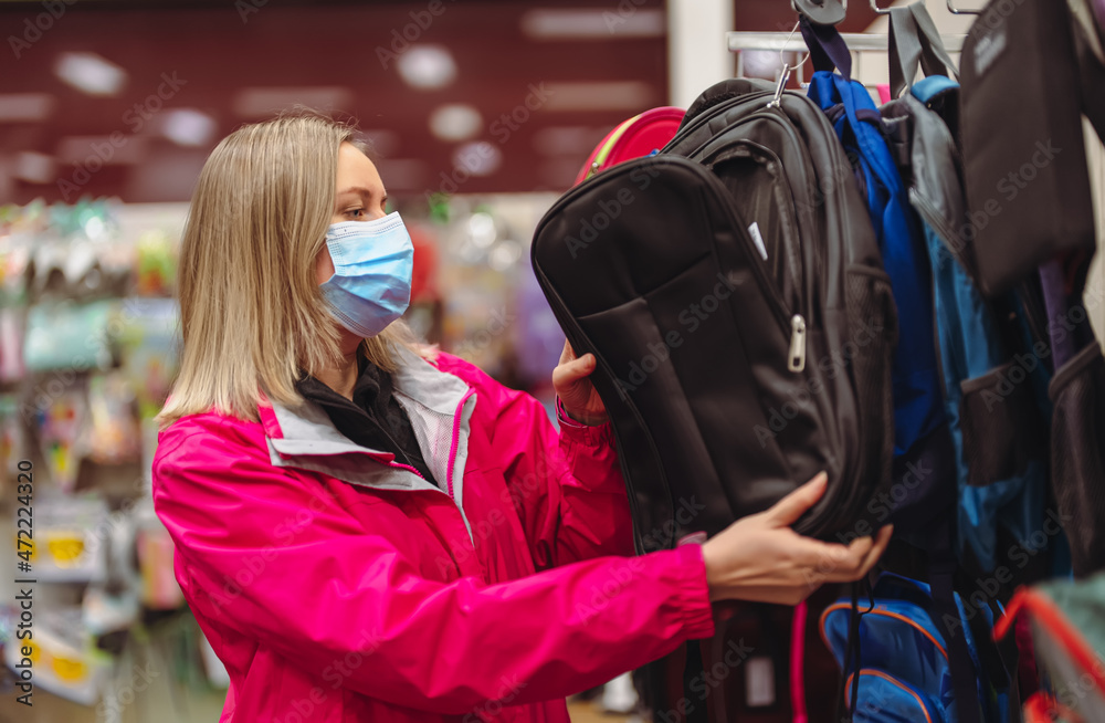 Woman in medical mask is choosing kid backpack for school. Woman in medical mask is choosing kid backpack for school.