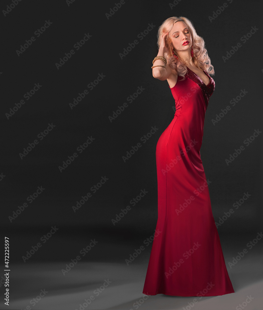woman in red dress studio portrait - sensual beautiful blonde model posing stands in a dark copy paste place background. Attractive sexy girl with long curly hair. Blurred details