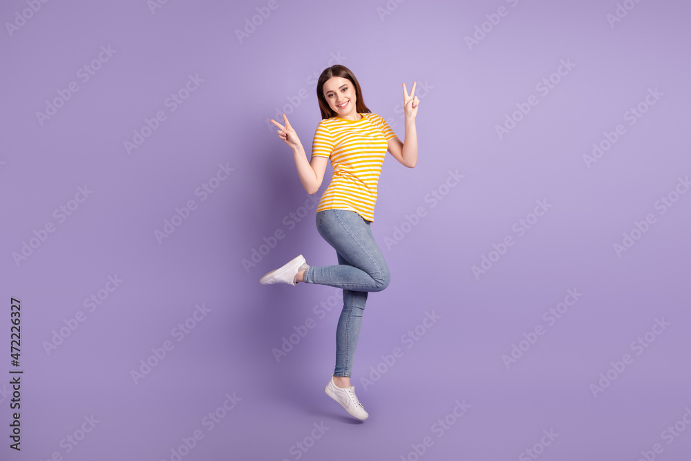 Full length profile side photo of young cheerful girl have fun jump show fingers peace v-symbol isolated over purple color background Full length profile side photo of young cheerful girl have fun jump show fingers peace v-symbol isolated over purple color background