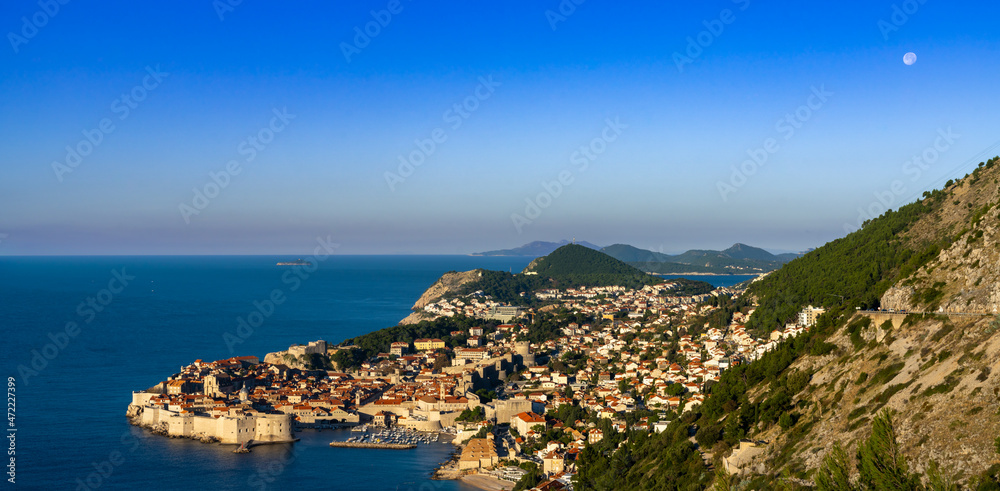 view of the historic city of Dubrovnik and the Adriatic Sea at sunrise with a full moon in the sky