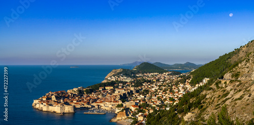 view of the historic city of Dubrovnik and the Adriatic Sea at sunrise with a full moon in the sky