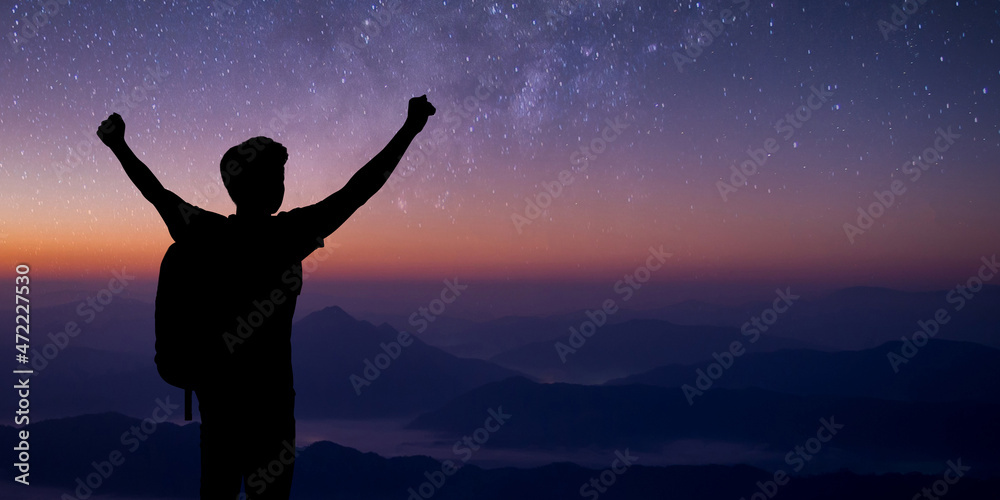 Silhouette of young traveler standing and open both arm watched night sky view, star and milky way alone on top of the mountain. He enjoyed traveling and was successful when he reached the summit.