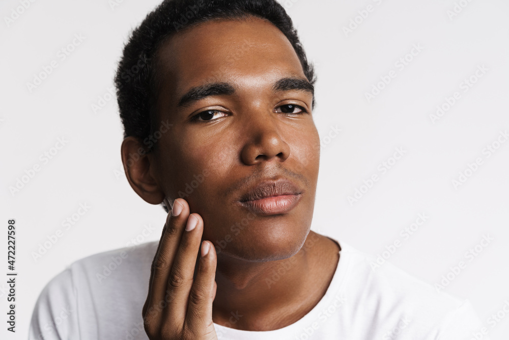 Young black man looking at camera while touching his skin Young black man looking at camera while touching his skin