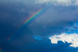 Colorful rainbow with dark storm clouds against a background of blue summer sky. Concept of change, hope.