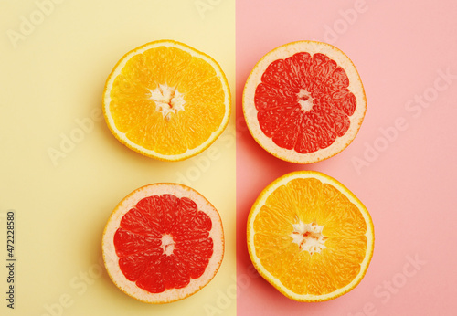 Halves of orange and grapefruit on geometric two colored soft yellow and pink background