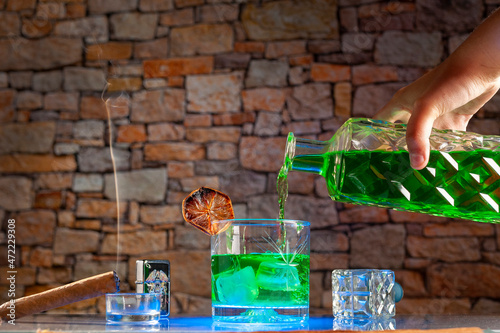 glass of green liquor with ice and an old bottle of green drink and cigar making smoke photo