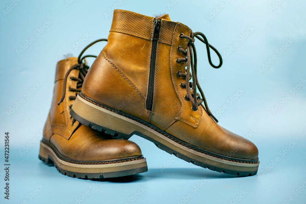 New pair of winter leather boots on a light blue background. One shoe is located on top of the other, front view. Fashionable concept. New pair of winter leather boots on a light blue background. One shoe is located on top of the other, front view. Fashionable concept.