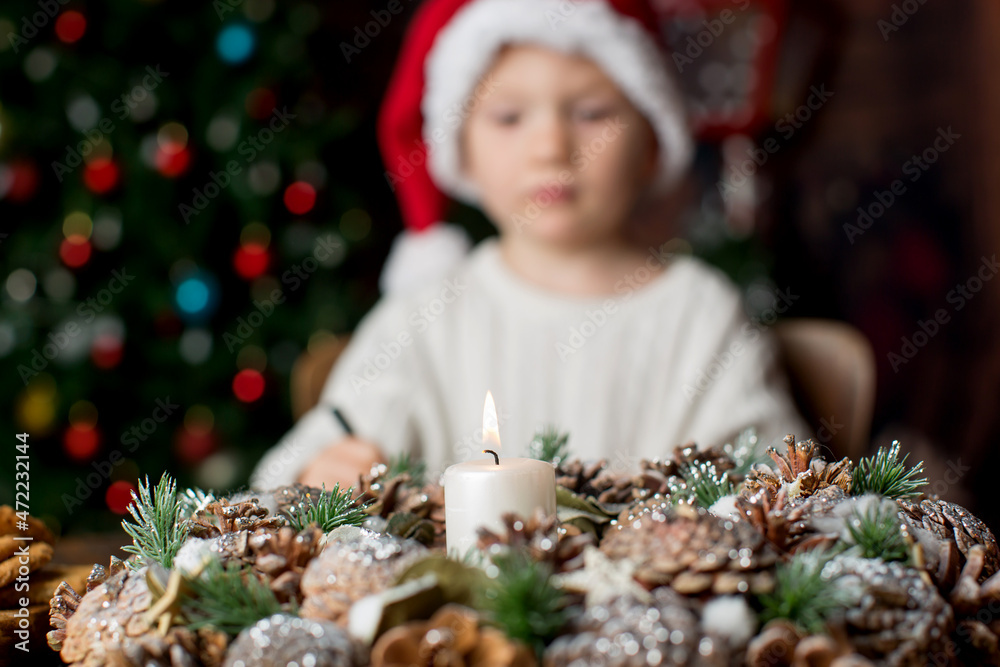 Advent wreath with burning candle in the middle, child writing letter in the background Advent wreath with burning candle in the middle, child writing letter in the background