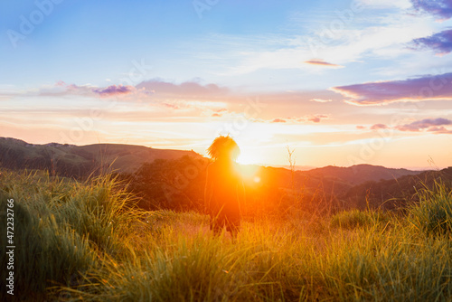 Retrato de un hombre con cabello rizado de espalda viendo y caminando al horizonte por el pasto de la montaña en un hermoso atardecer photo