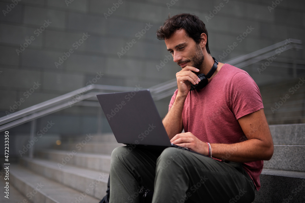 Handsome man working with laptop on city street. Man using his laptop while sitting on stairs outdoors.. Handsome man working with laptop on city street. Man using his laptop while sitting on stairs outdoors..
