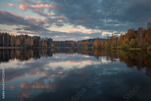 Sunset sky and forest is reflected in the water of the lake in the autumn evening