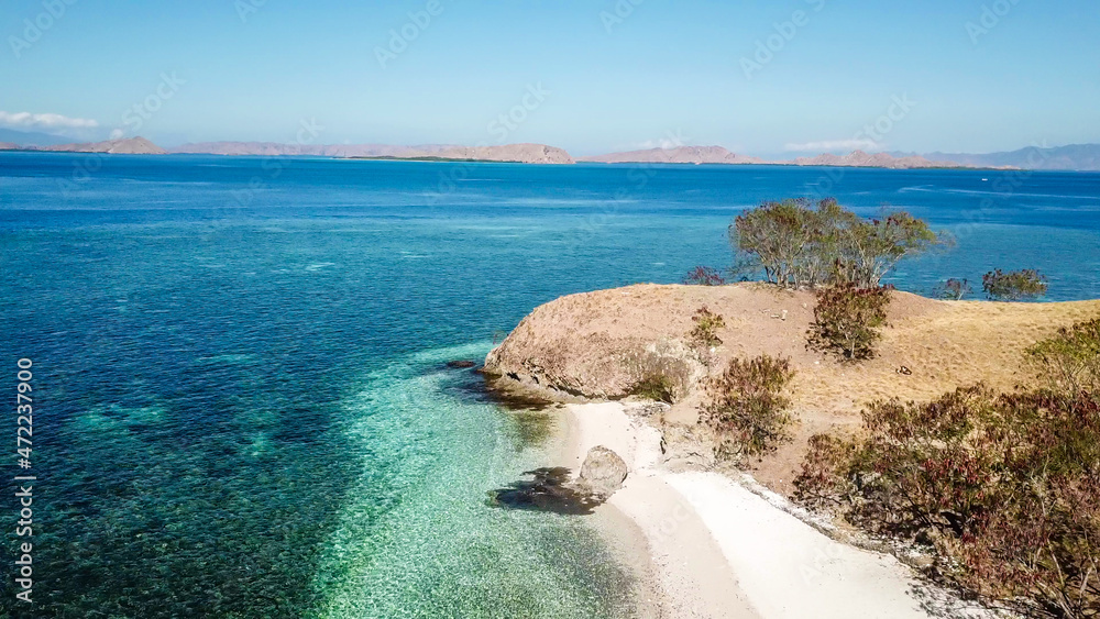 Top down drone shot of a paradise island with some boats anchored around in Komodo National Park, Flores, Indonesia. Brownish island turns into white sand beach and further into green and navy sea
