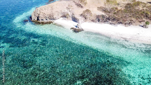 A drone shot of a paradise island in Komodo National Park, Flores, Indonesia. Brownish island turns into white sand beach and further into turquoise and navy blue sea. Steep slopes of the island