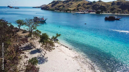 Top down drone shot of a paradise island with some boats anchored around in Komodo National Park, Flores, Indonesia. Brownish island turns into white sand beach and further into green and navy sea