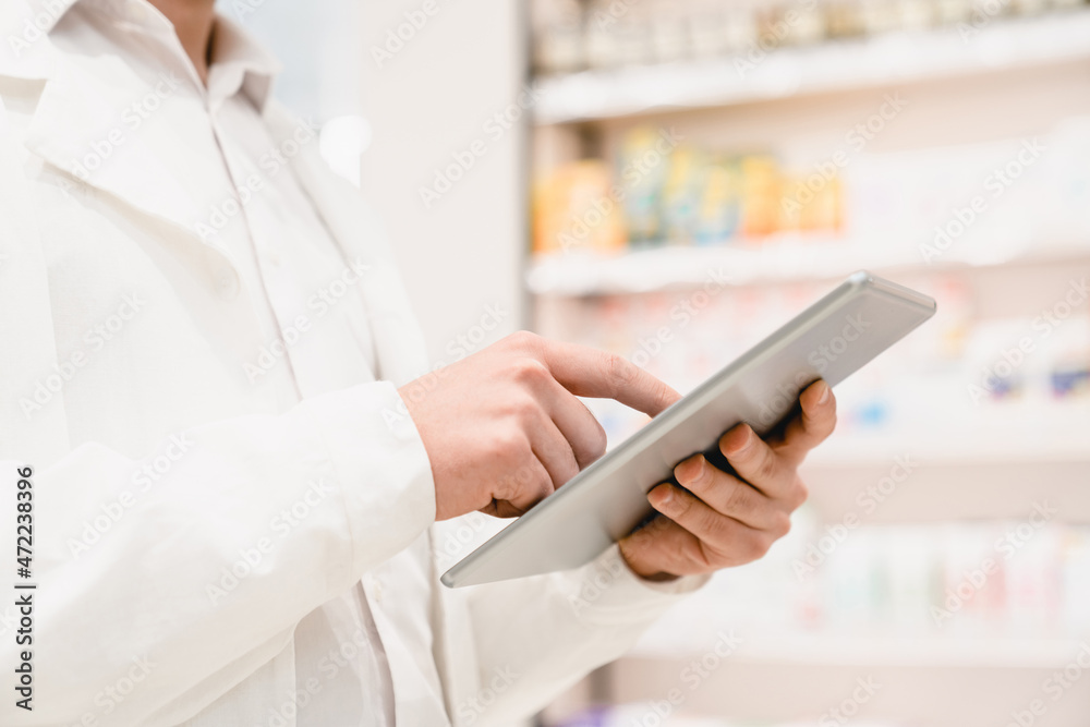 Closeup cropped image of druggist pharmacist using digital tablet for checking expiration date, side effects, active substance of drugs, pills, medicines in pharmacy Closeup cropped image of druggist pharmacist using digital tablet for checking expiration date, side effects, active substance of drugs, pills, medicines in pharmacy