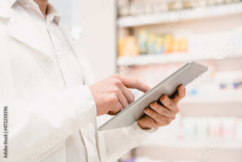 Closeup cropped image of druggist pharmacist using digital tablet for checking expiration date, side effects, active substance of drugs, pills, medicines in pharmacy