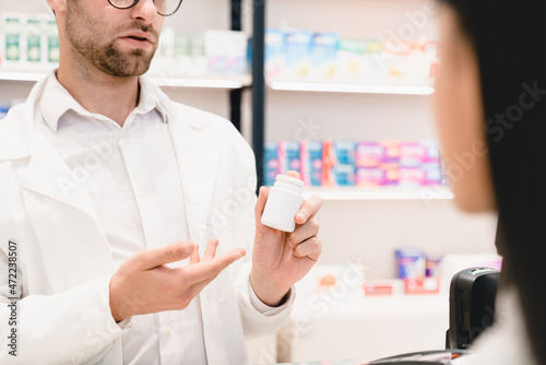 Male pharmacist druggist advising talking telling about new medicines pills remedies  side effects to a female customer patient holding a jar with mockup. Pharmacy consultation