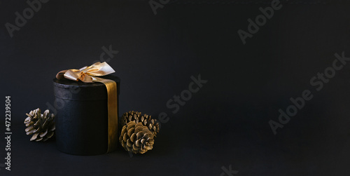 Black gift box with golden bow on black background for christmas and new year concept